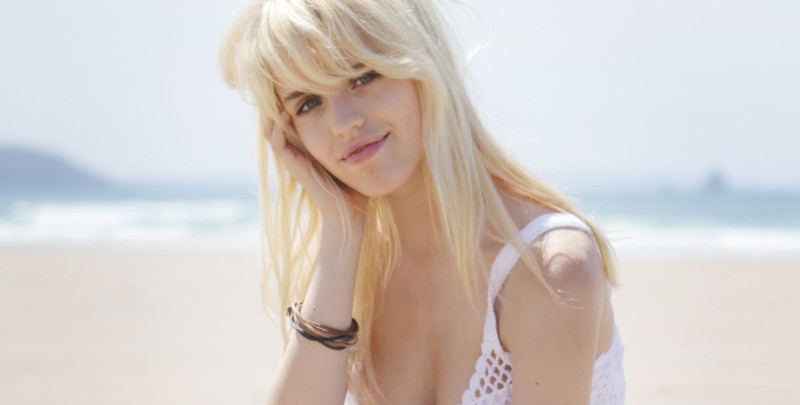 Een blondje in zomerjurkje, gaat naakt op het strand