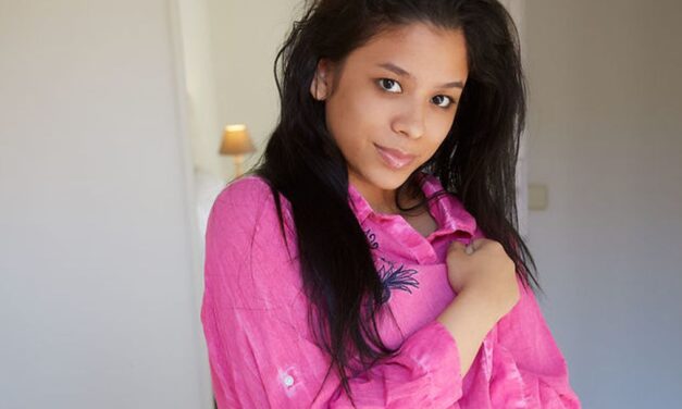 Karin Torres, een roze overhemd en naakt op bed